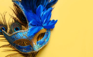Venedik karnaval maskesi ve tavus kuşu tüylerinin üst görüntüsü. Sarı arkaplanda yazılı metin için yer var. Karnaval konsepti