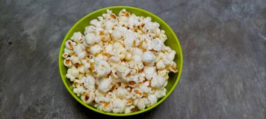 Beton bir arka planda yeşil bir kasede taze patlamış mısır..