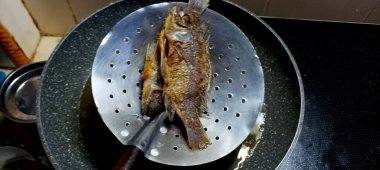 Kavrulmuş tilapia balığı. Mutfak ocağında yağlı bir tavada pişiyor..
