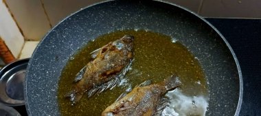 Kavrulmuş tilapia balığı. Mutfak ocağında yağlı bir tavada pişiyor..