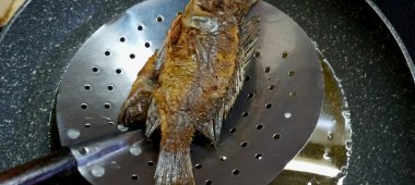 Kavrulmuş tilapia balığı. Mutfak ocağında yağlı bir tavada pişiyor..