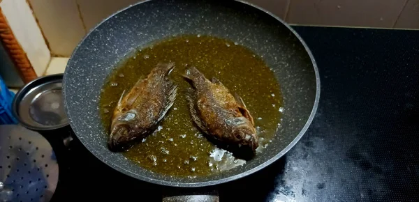Kavrulmuş tilapia balığı. Mutfak ocağında yağlı bir tavada pişiyor..
