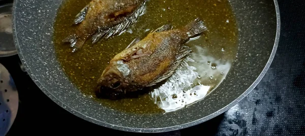 Kavrulmuş tilapia balığı. Mutfak ocağında yağlı bir tavada pişiyor..