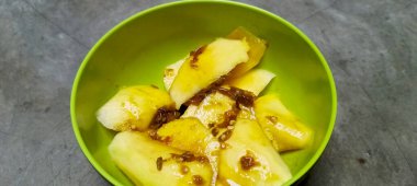 Tatlı, ekşi ve baharatlı palmiye şekeri soslu ince dilimlenmiş taze meyve. Gri beton zemin.