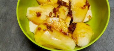 Tatlı, ekşi ve baharatlı palmiye şekeri soslu ince dilimlenmiş taze meyve. Gri beton zemin.