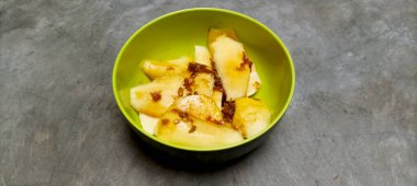 Tatlı, ekşi ve baharatlı palmiye şekeri soslu ince dilimlenmiş taze meyve. Gri beton zemin.