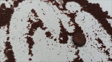 Beyaz arka planda kahve telveleriyle çevrili tek bir kavrulmuş kahve çekirdeği.