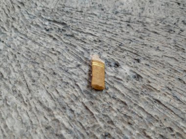 Kullanılmış mini puro ya da sigara filtresinin yakın plan fotoğrafı sert, desenli gri beton kaldırıma atılmış..