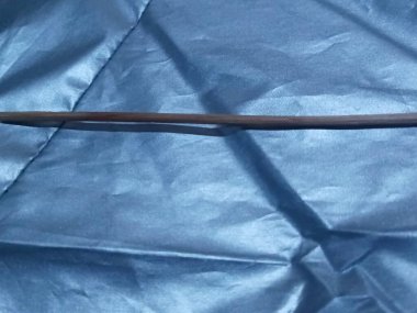 Tek bir doğal bambu satay çubuğunun detaylı makro fotoğrafı parlak, buruşuk mavi kumaş bir yüzey üzerinde duruyor..