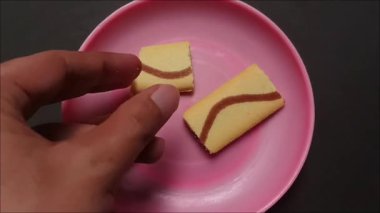 Çikolata kremalı ve dalgalı bir tasarımı olan yumuşak bir mini pasta tutan bir elin görüntüsü..