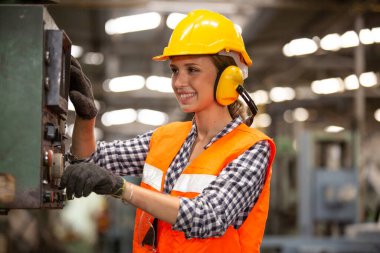 Elektronik kontrol panelinde düğmelere basan ve modern fabrikada çalışan makine birimlerine bakarken kameraya bakan gülümseyen işçilerin portresi, fabrikada bir cnc makinası çalıştıran kadın mühendisler