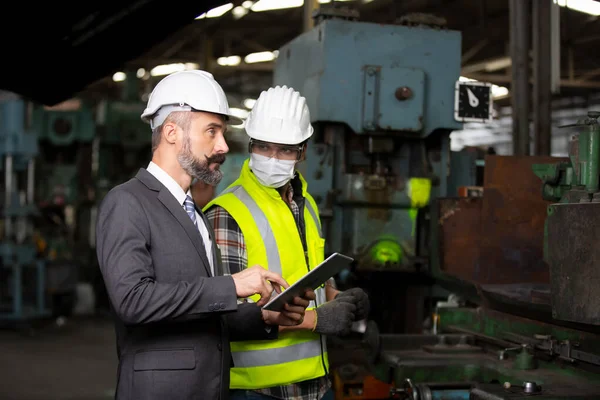 Erkek Endüstriyel Mühendisler Fabrika İşçisiyle konuşuyor. Ağır Sanayi Üretim Tesisinde çalışıyorlar..