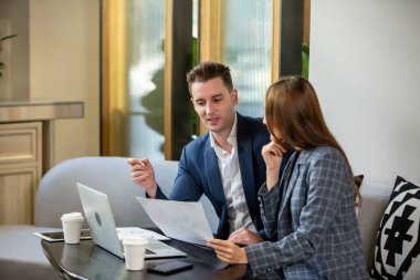 Kafede oturmuş laptopla yeni bir proje üzerinde çalışan iki iş adamı. Not alan genç iş kadını ve dizüstü bilgisayarda çalışan iş adamı.