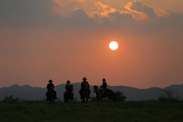 乗馬中のグループカウボーイ 彼の馬に座ってカウボーイのグループのシルエットまたは日没時にカウボーイ乗馬のシルエット — ストック写真