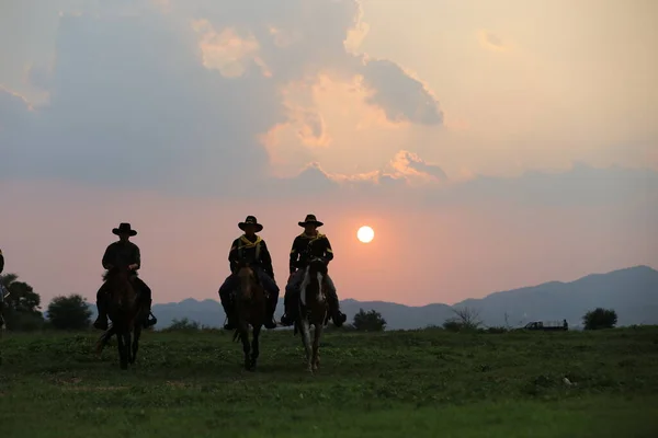 日没に向かって銃を持って騎乗するカウボーイ — ストック写真