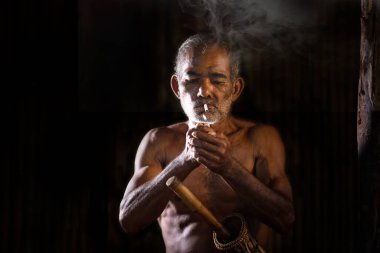 Siyah arka planda sigara içen yaşlı bir adamın kasvetli ve somurtkan görüntüleri.