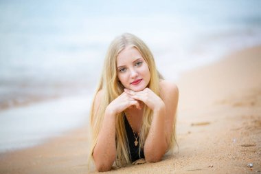 Tropikal plajda uzanan bikinili, siyah mayo giymiş mutlu bir kadın yaz tatilinin tadını çıkarıyor ve mavi gökyüzüne karşı beyaz kumlara uzanıyor. Tatil, tatil, yaşam tarzı konsepti. Kopyalama alanı