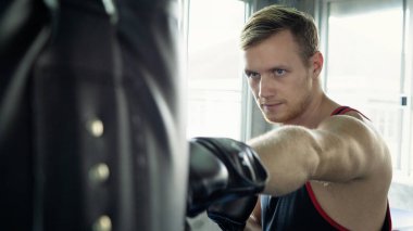 Yong erkek boksör boks stüdyosunda büyük bir kum torbasına vuruyor. Sıkı çalışan bir boksör..