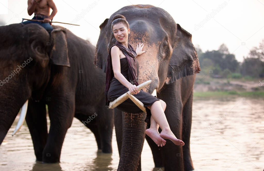 Portrait Of Smiling Woman Sitting on  ivory of Elephant In the river at Thailand.