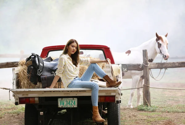 Portrait of Woman sitting on truck in farm with horse on field