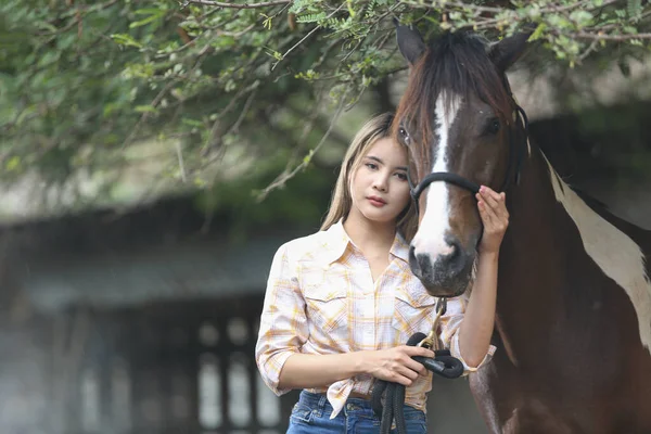 A woman in a cowgirl outfit standing with a horse at a cattle farm.