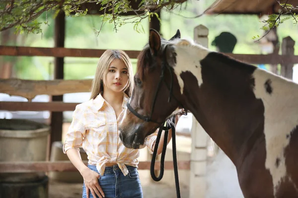 A woman in a cowgirl outfit standing with a horse at a cattle farm.