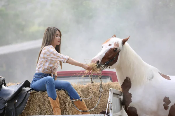 A woman in a cowgirl outfit standing with a horse at a cattle farm.