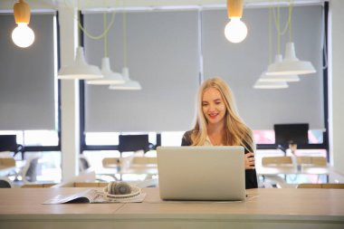 İş yerinde dizüstü bilgisayar kullanan gülümseyen bir kadın, izleyici çekmek ve içerik yaratmak isteyen küçük işletmeler için iş yerinde yeni pazarlama teknolojisi benimseyebilir. Serbest Çalışan Konsepti.