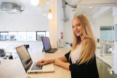 İş yerinde dizüstü bilgisayar kullanan gülümseyen bir kadın, izleyici çekmek ve içerik yaratmak isteyen küçük işletmeler için iş yerinde yeni pazarlama teknolojisi benimseyebilir. Serbest Çalışan Konsepti.