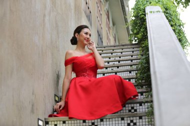 Güzel kırmızı elbiseli genç Asyalı kadın gülümseyerek kameraya bakıyor. Moda modeli, gelin ya da düğün öncesi konsept.