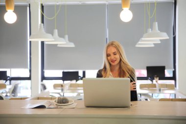 Bilgisayarla çalışan güzel genç bir kadın konsantre olmuş ve gülümsüyor.