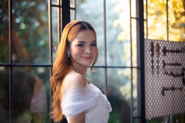 Gelinlik giymiş, saçları kıvırcık, güzel, çekici, gülümseyen bir kadın resmi..