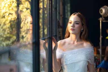 Gelinlik giymiş, saçları kıvırcık, güzel, çekici, gülümseyen bir kadın resmi..