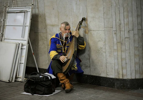 En gammal man i ukrainska nationella kläder, gatumusiker, spelar infödda musikinstrument kobza i den tomma tunnelbanan passage — Stockfoto