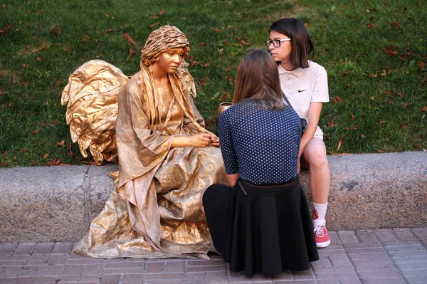 İki kız kaldırımda oturan sokak aktörüyle iletişim kuruyor. 1 Haziran 2012. Kiev, Ukrayna