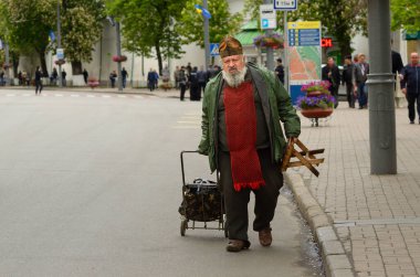 Yaşlı bir ortodoks keşiş sokakta araba sürüp katlanır sandalye çekiyor. 9 Mayıs 2018. Kiev, Ukrayna