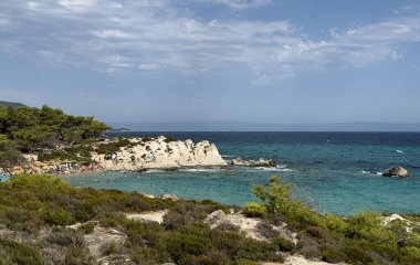 Kavourotrypes plajı manzarası, resmi çıplaklar plajı yaz güneşli mavi gökyüzü deniz taşları, güneşlenen insanlar. 2025 yılı. Sithonia Yarımadası, Yunanistan