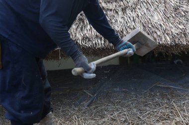 Bir zanaatkar sazdan çatıyı tamir ediyor.