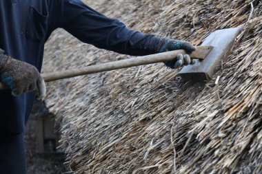Bir zanaatkar sazdan çatıyı tamir ediyor.
