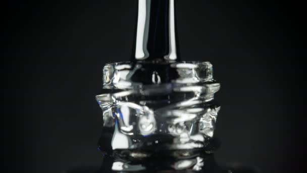 Esmalte de uñas de gel transparente con una botella abierta y una gota goteando en un frasco con un cepillo en el salón de belleza. Fondo negro. Primer plano. — Vídeos de Stock