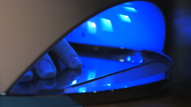 Primer plano de las uñas azules femeninas y la piel debido a la luz azul de la lámpara led. Tecnología para el curado y secado de manicura lámpara UV cubierta con gel pulido de moda moderna. — Vídeos de Stock