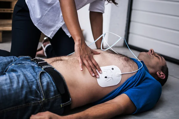 Ragazza che applica pastiglie defibrillatore a un ragazzo privo di sensi — Foto Stock