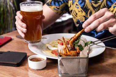 Kızarmış kalamar, domates salatası, kırmızı soğan, kızarmış kırmızı kefal balığı, bir bardak bira ve ahşap masada sos. Bir tabak mürekkep balığının üzerinde çatal ve bira tutan erkeklerin elleri..