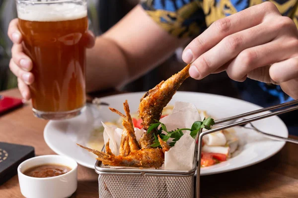 Kızarmış kırmızı kefal balığı ve ahşap bir masada bira bardağı. Erkeklerin elleri ahşap masada kırmızı bir balık ve bira tutuyor..
