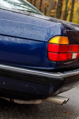 Yağmurdaki klasik mavi arabanın ayrıntıları su damlacıkları, krom süslemeler, arka farlar, egzoz boruları ve sonbahar yolundaki kapı koluyla birlikte.