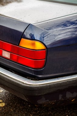 Yağmurdaki klasik mavi arabanın ayrıntıları su damlacıkları, krom süslemeler, arka farlar, egzoz boruları ve sonbahar yolundaki kapı koluyla birlikte.