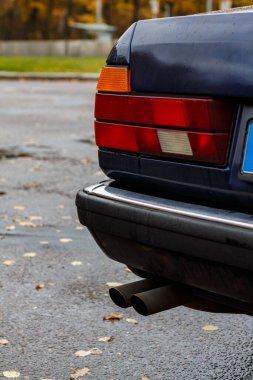 Yağmurdaki klasik mavi arabanın ayrıntıları su damlacıkları, krom süslemeler, arka farlar, egzoz boruları ve sonbahar yolundaki kapı koluyla birlikte.