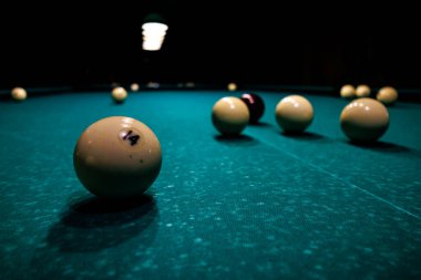 Bilardo masasında, karanlık bir odada hafif lambaların altında duran toplar, yalnızlık, odaklanma ve sessiz oyun ortamı yaratıyor.