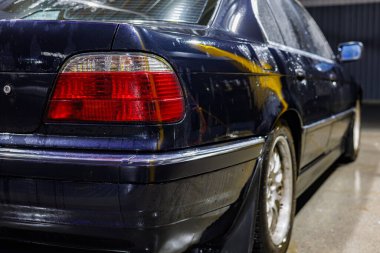 Gece araba yıkamada siyah sedan. Vücudunda ve ön camında su damlacıkları, ıslak zeminde neon yansımaları ve atmosferik ışıklandırma endüstriyel, sinematik bir hava yaratıyor.