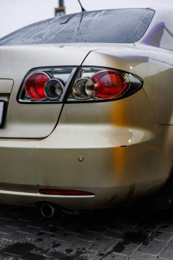 Fenerinde yağmur damlacıkları olan parlak gümüş renkli bir araba, parlak ışıklandırılmış bir oto yıkama istasyonuna yakın plan çekimde yakalandı.